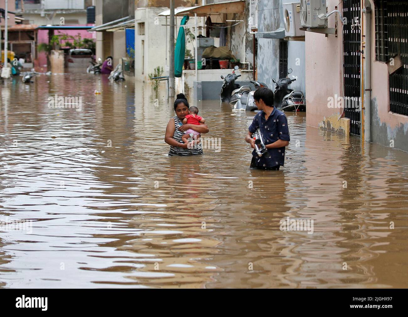 A woman carries her infant through a water-logged neighbourhood after her house was inundated with flood water following heavy rains in Ahmedabad, India, July 11, 2022. REUTERS/Amit Dave Stock Photo