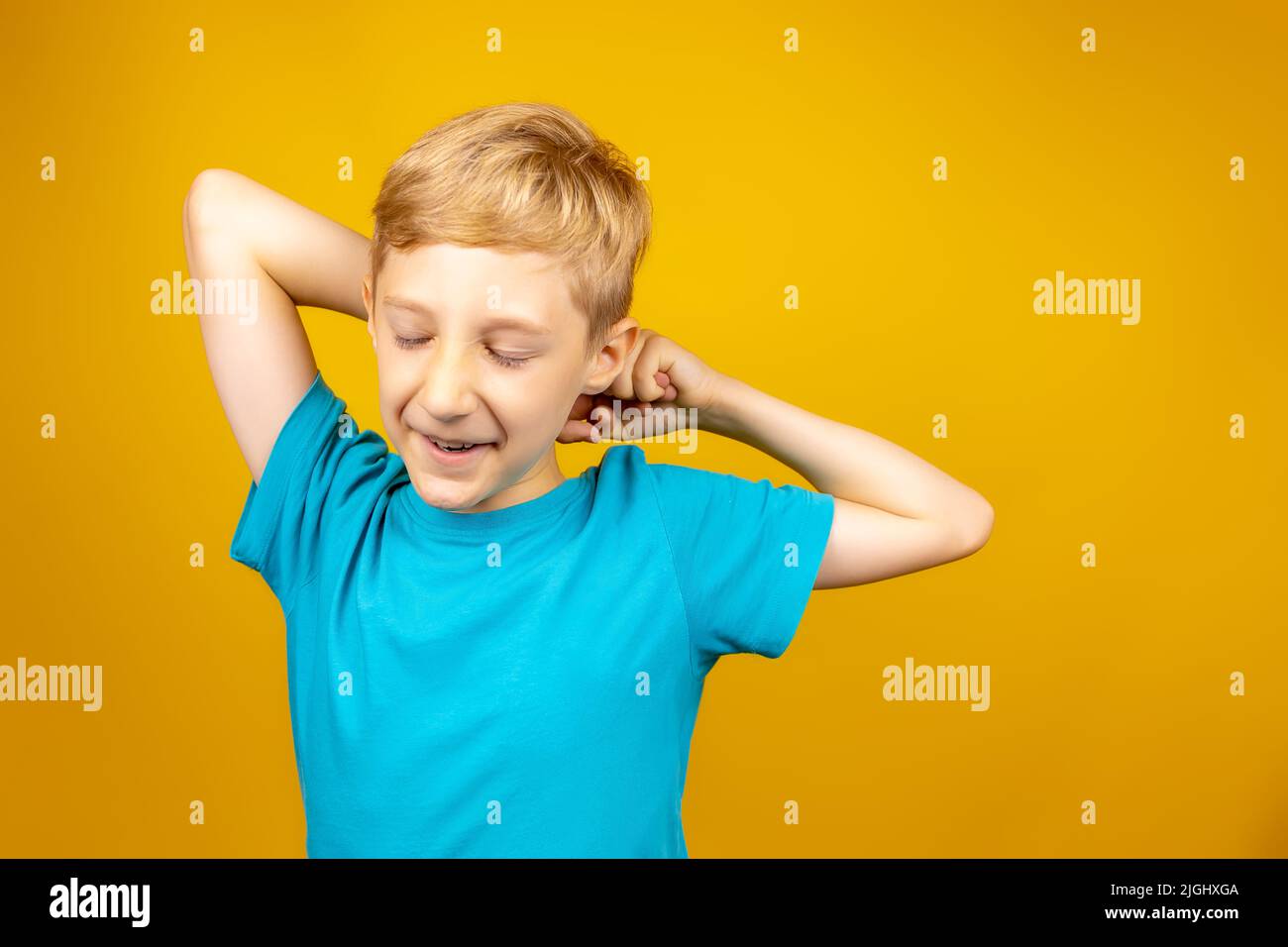 a boy on a yellow background dressed in a blue T-shirt stretches and closes his eyes Stock Photo