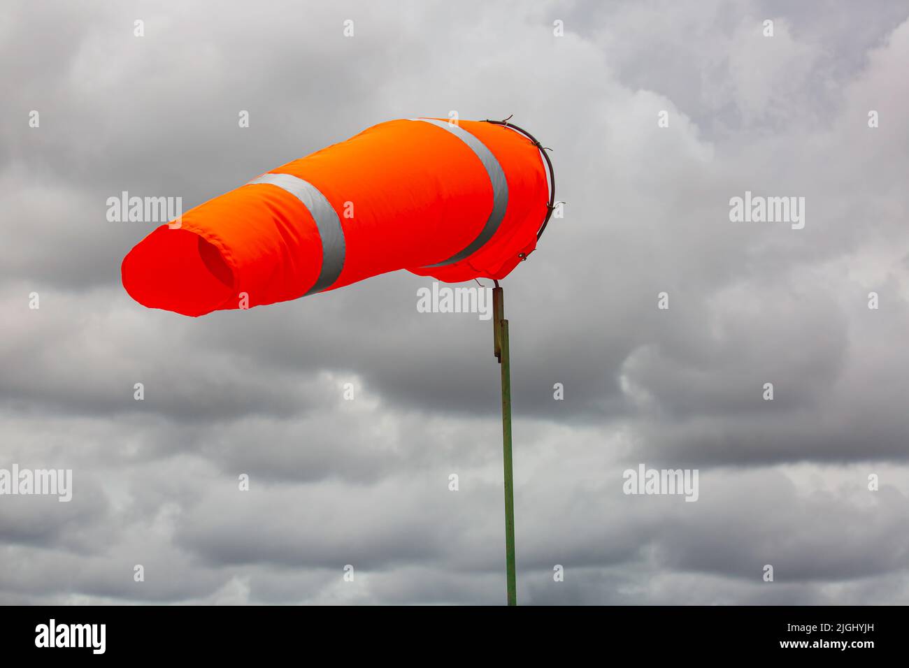 Windsock indicator of wind on tank chemical cone indicating wind direction and force. Horizontally flying windsock (wind vane) with cloud sky in the b Stock Photo