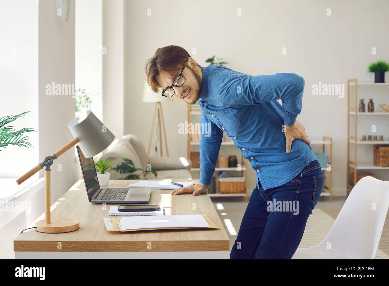 Male office worker experiences severe back pain caused by prolonged sitting in wrong position. Stock Photo