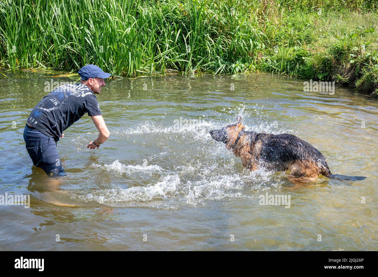 Overcote, Over, Cambridgeshire UK, 11th July 2022. Peter and his German Shepherd dog Mia cool down in the River Great Ouse in the UK heatwave. Amber warnings for high temperatures have been issued in the east of England today as temperatures are forecast to be above 30 degrees centigrade. The UK weather is expected to be hot and sunny most of the week with the potential to break the record for the hottest day at the weekend. Credit: Julian Eales/Alamy Live News Stock Photo