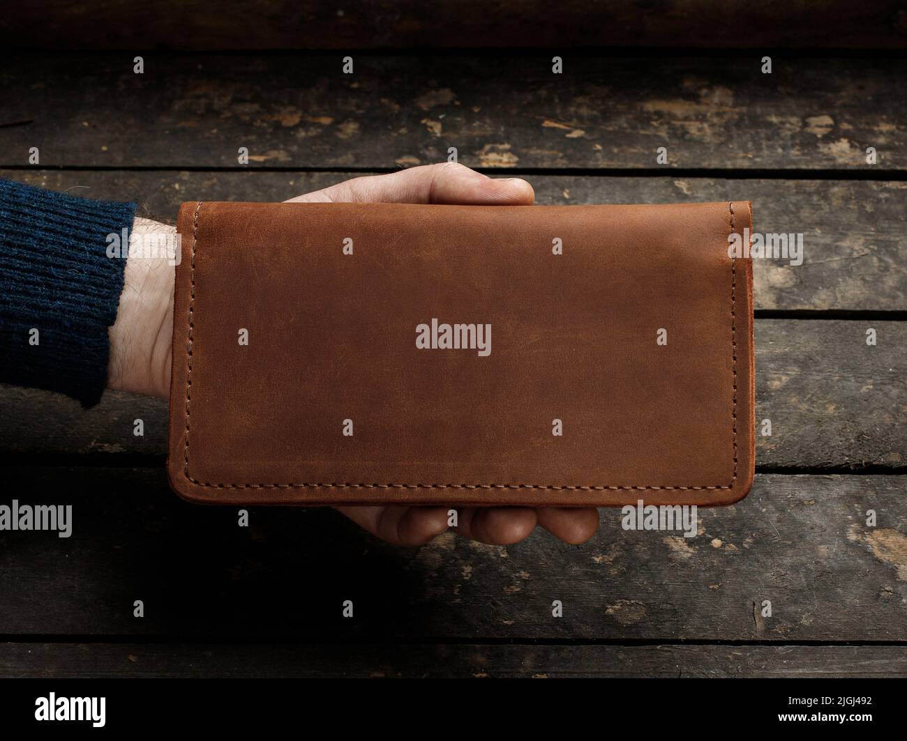 Leather red men's wallet in a man's hand on a vintage wooden background. Flat lay. Place for text. Copyspace Stock Photo
