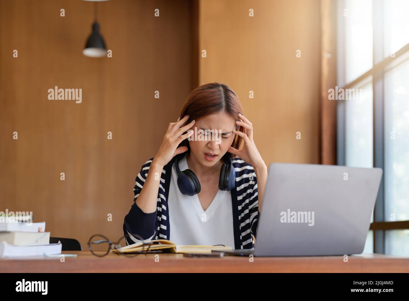 Stressed Asian woman cover her face with hand and feel upset from work in front of laptop computer on desk at office,Stress office lifestyle concept. Stock Photo