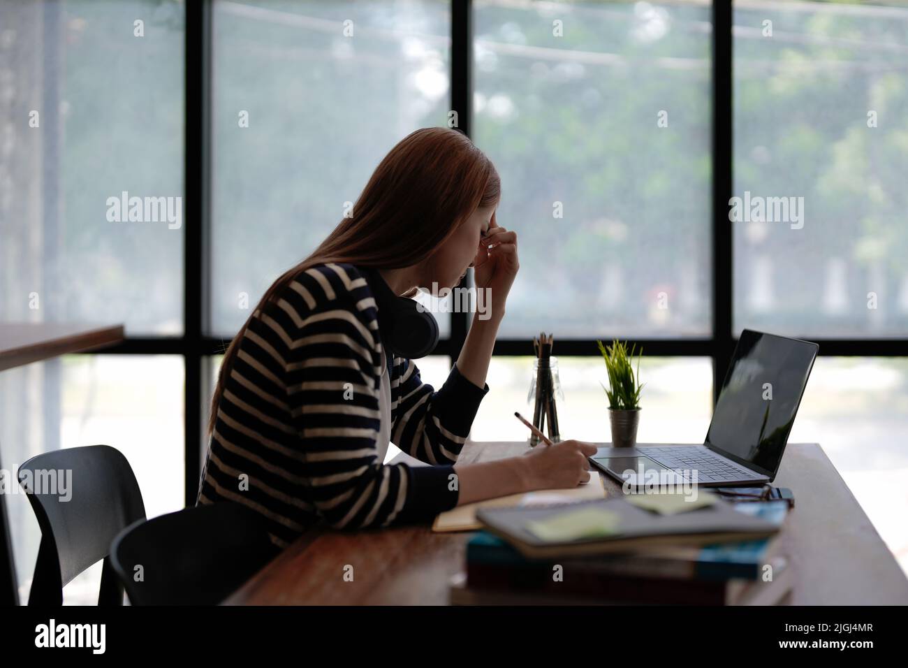 Stressed Asian woman cover her face with hand and feel upset from work in front of laptop computer on desk at office,Stress office lifestyle concept. Stock Photo