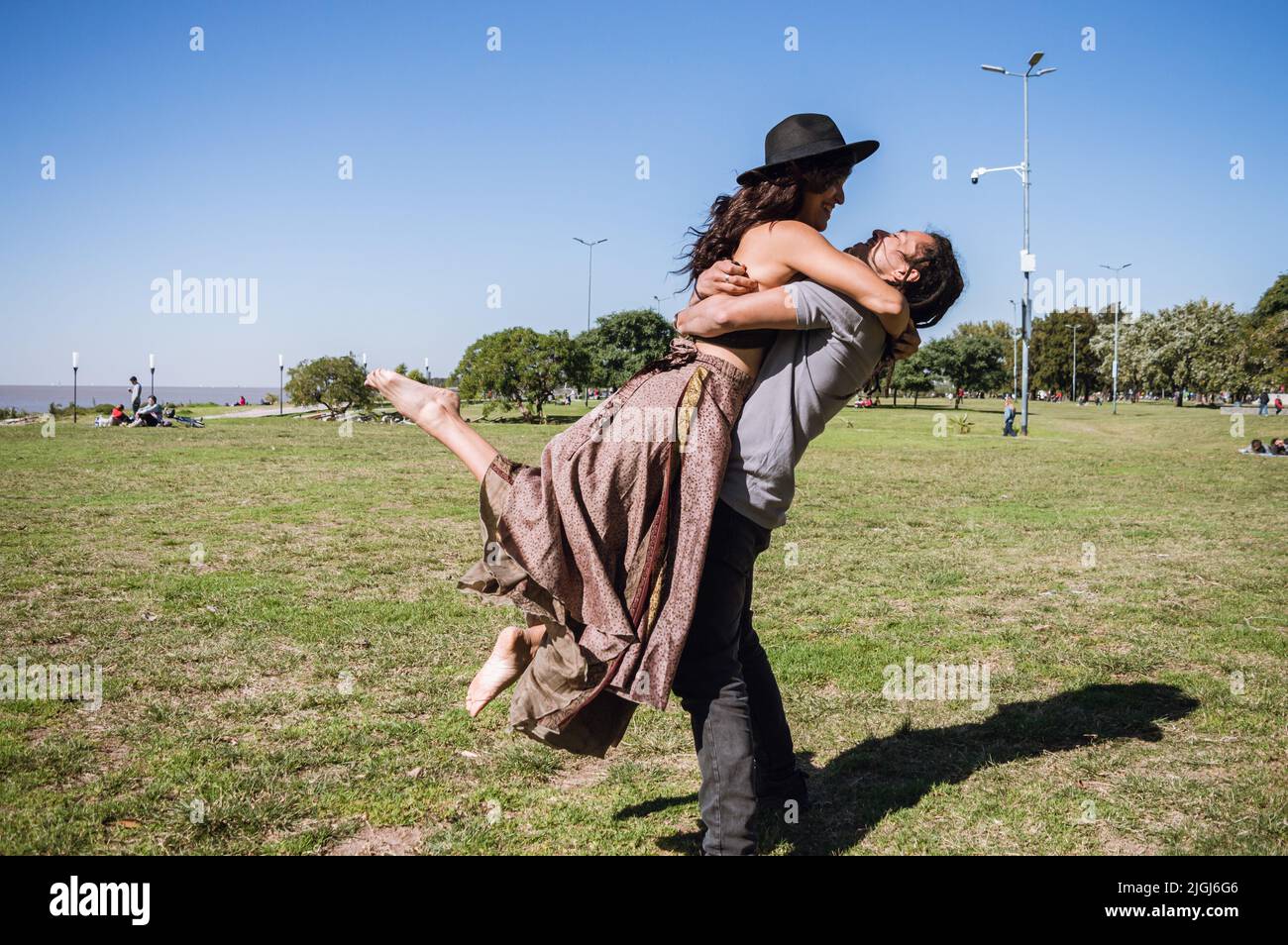 young caucasian latin couple on the beach, playing standing outdoors, man carries his girlfriend in his arms while they see each other from the front. Stock Photo