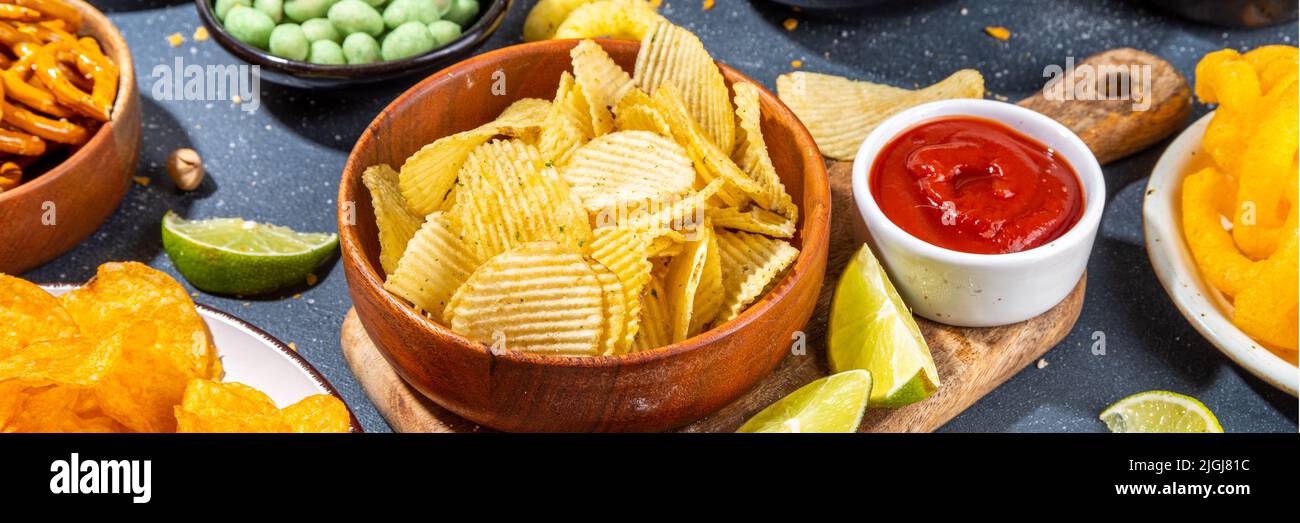 Various unhealthy salty bar snacks set. Dark grey table background with