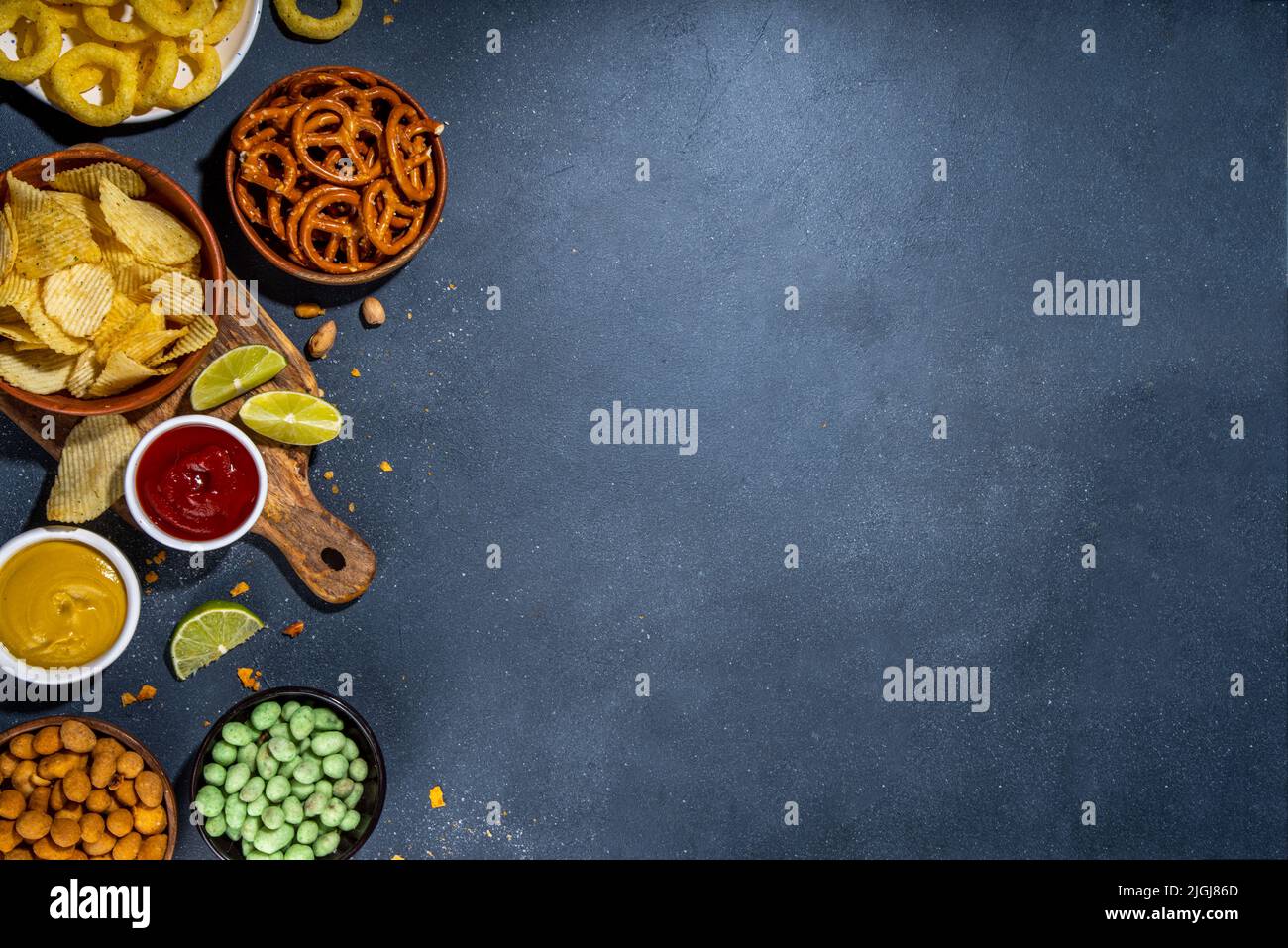 Various unhealthy salty bar snacks set. Dark grey table background with