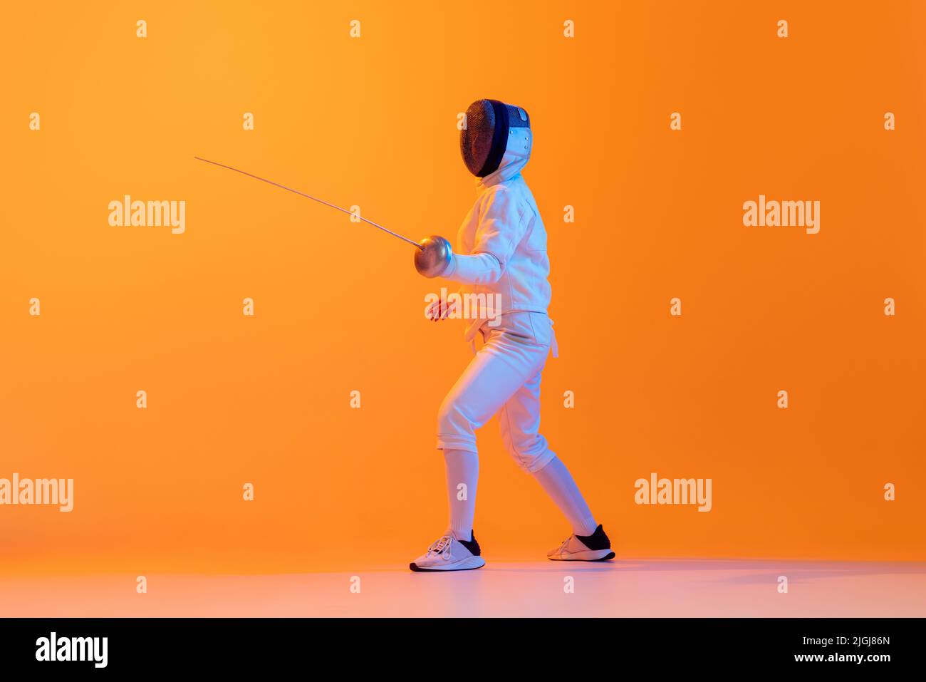 Studio shot of professional fencer in white fencing costume and mask in