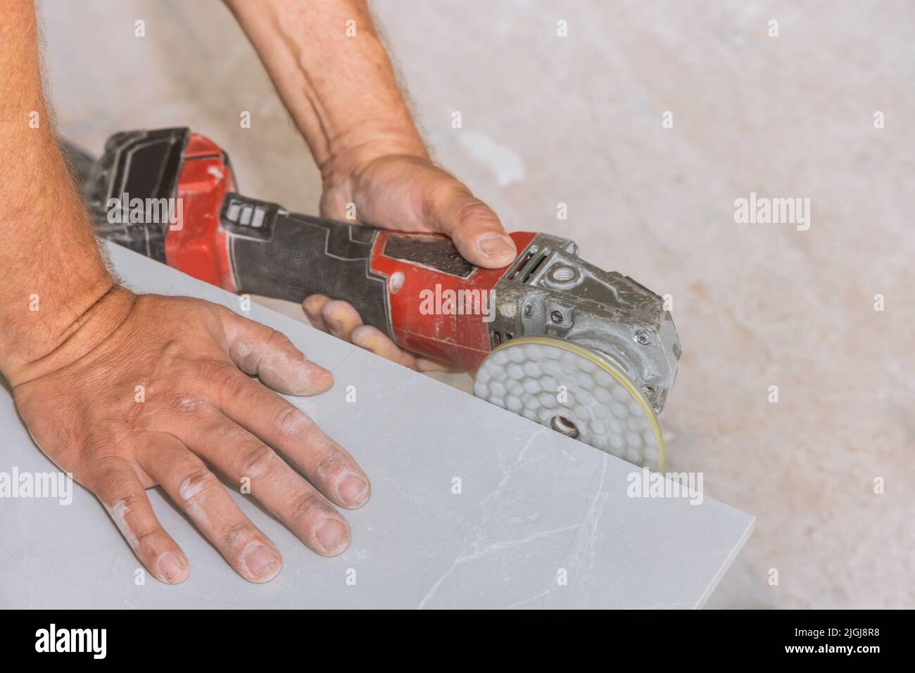 A worker polishes the corners of cut tiles with a polishing disk with diamond on an angle grinder Stock Photo