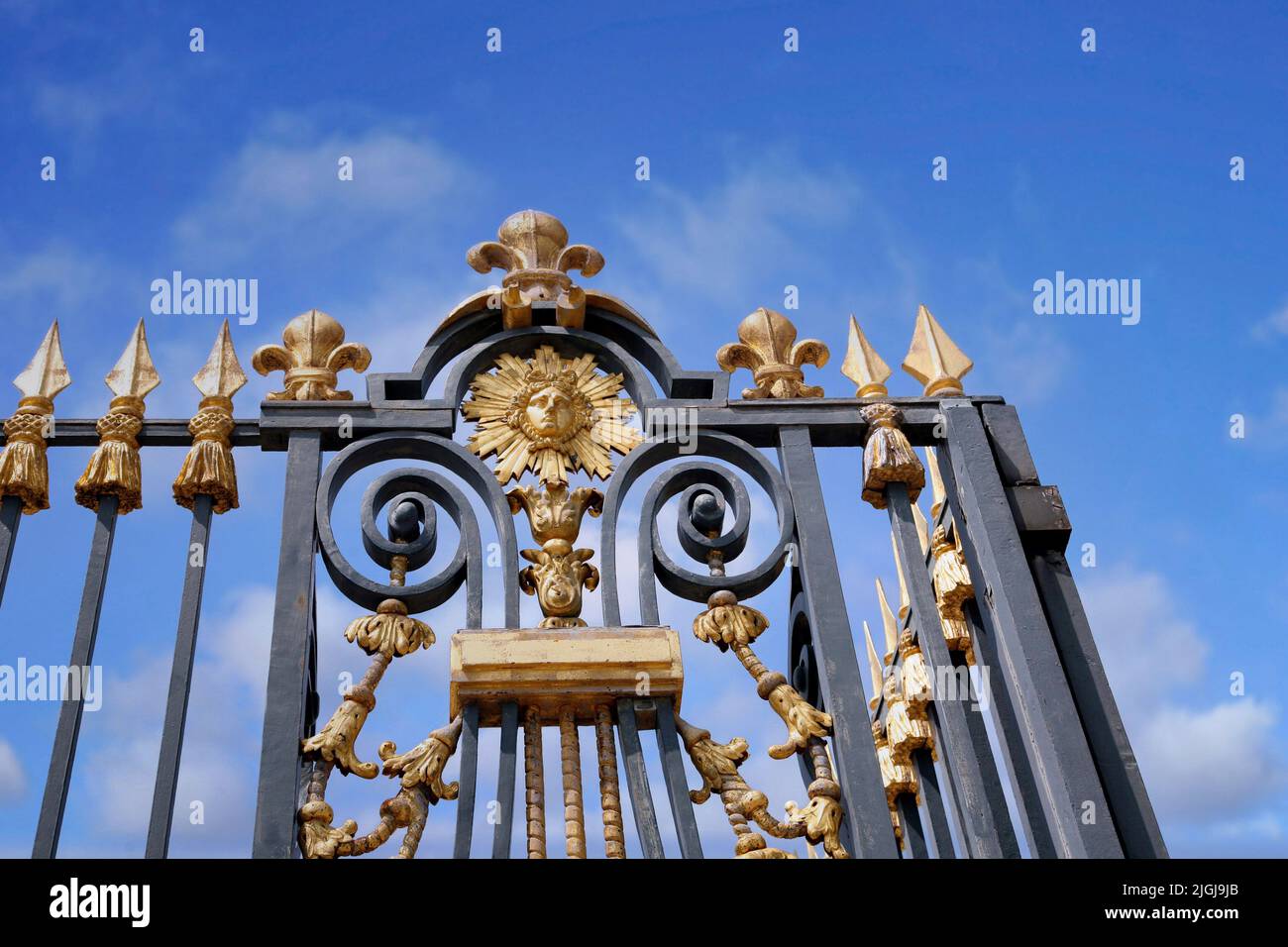 Gilded fence at the former royal palace at Versailles, with Louis XIV depicted as the Sun King Stock Photo