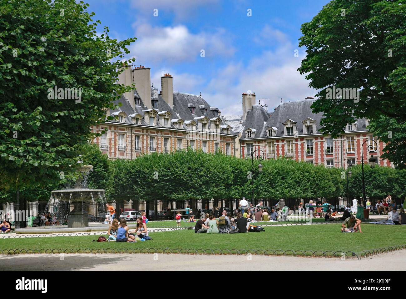 Families with children relax on the lawn of the Place des Vosges gardens on a warm summer day Stock Photo
