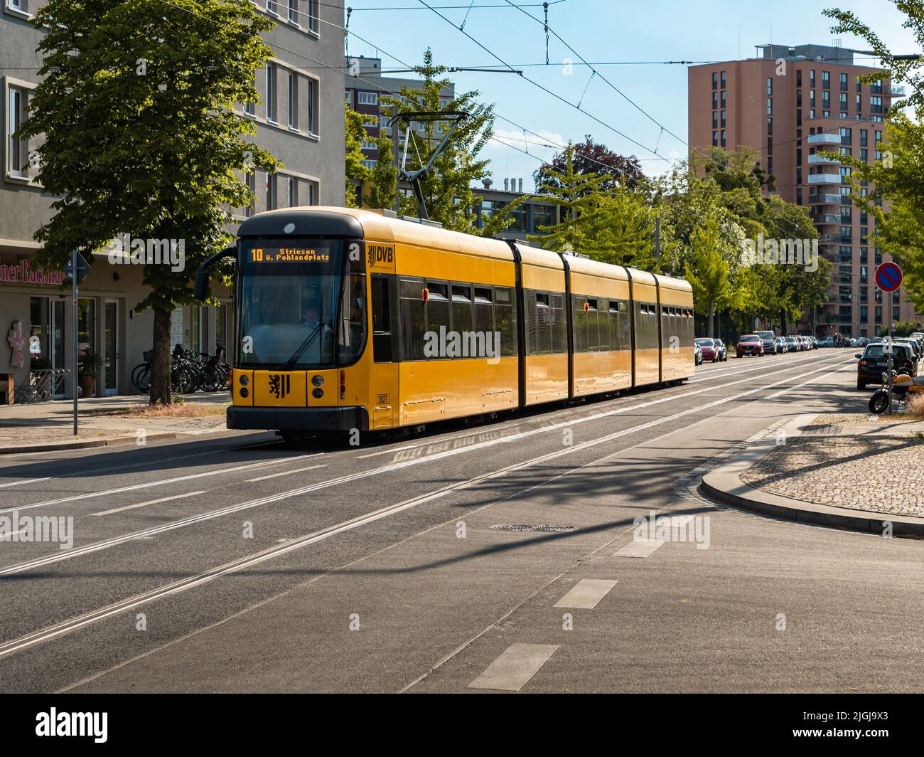 Tram of the DVB in the city. Empty street with a yellow cable car in Saxony. Public transportation on rails. Vehicle of the Dresdner Verkehrsbetriebe. Stock Photo