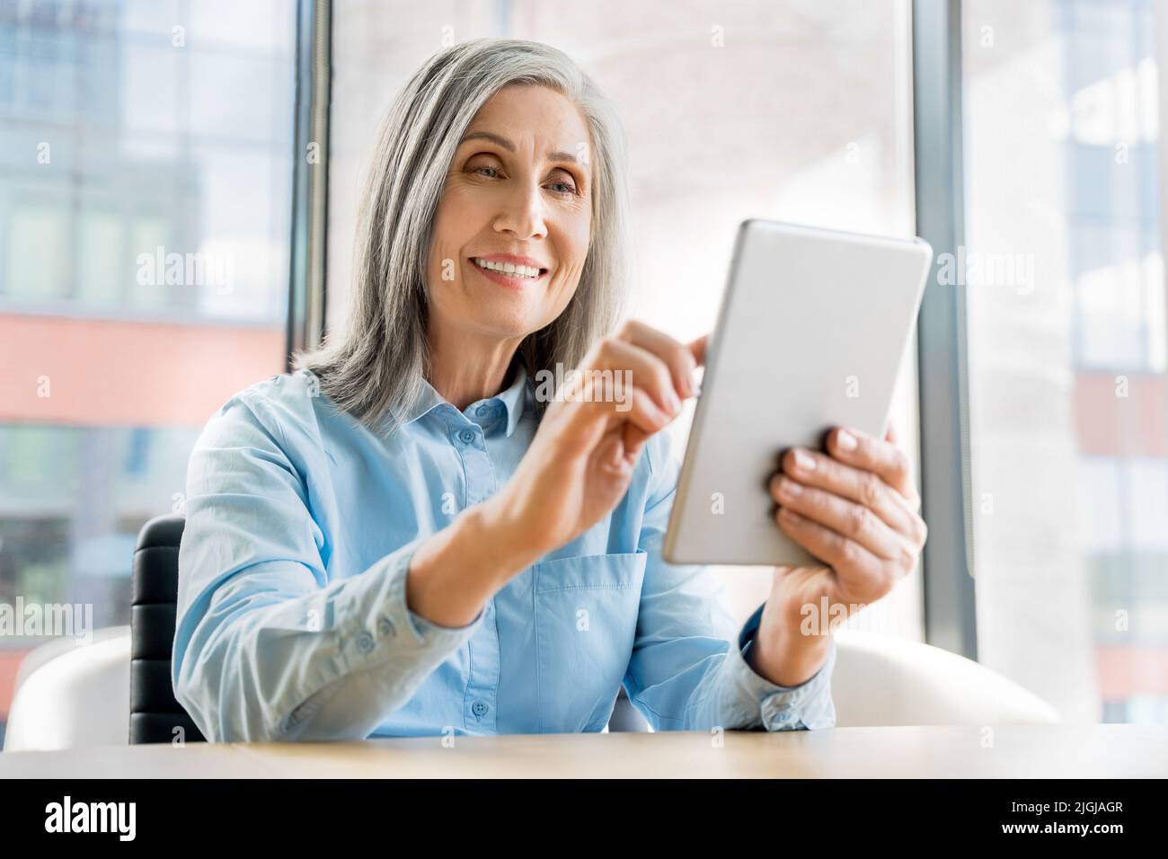 60s older mature woman sit in office and use digital tablet Stock Photo