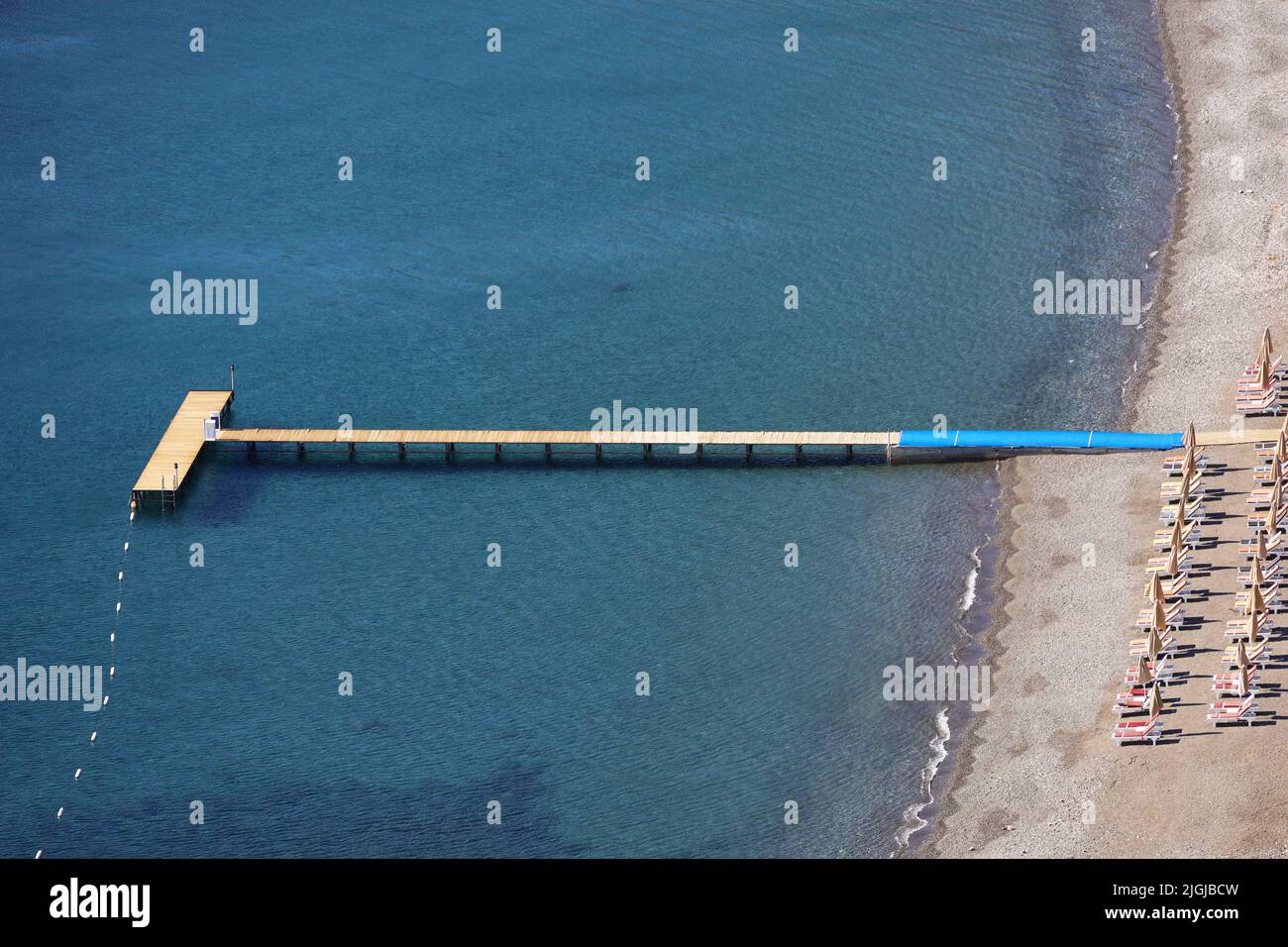 Aerial view to Mediterranean sea, wooden pier and beach with empty deck chairs. Coast with transparent water, summer resort Stock Photo