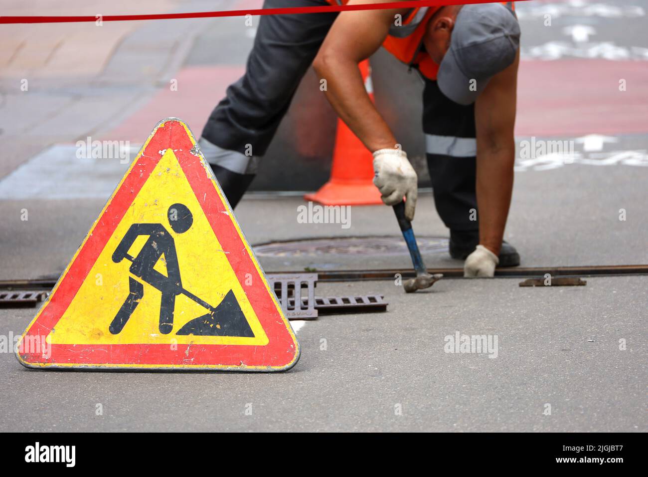 Road works sign, worker of municipal services repairs drainage system. Wastewater treatment, orange roadblock cones on the city street Stock Photo