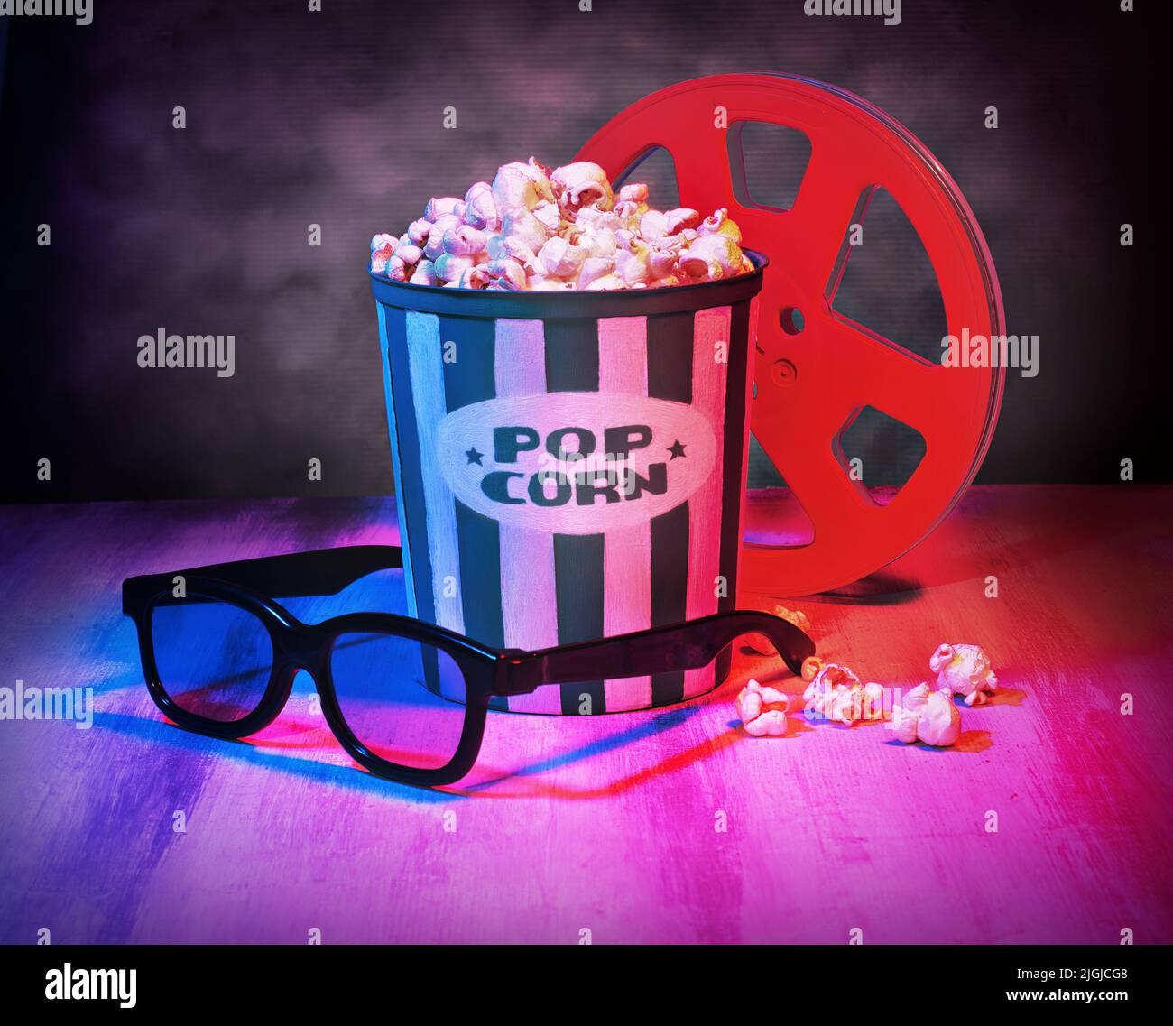 Cinema movies concept with a pop corn bucket, 3D glasses and film tape reel. Movie night template symbol table top shot, with a purple retro aesthetic Stock Photo