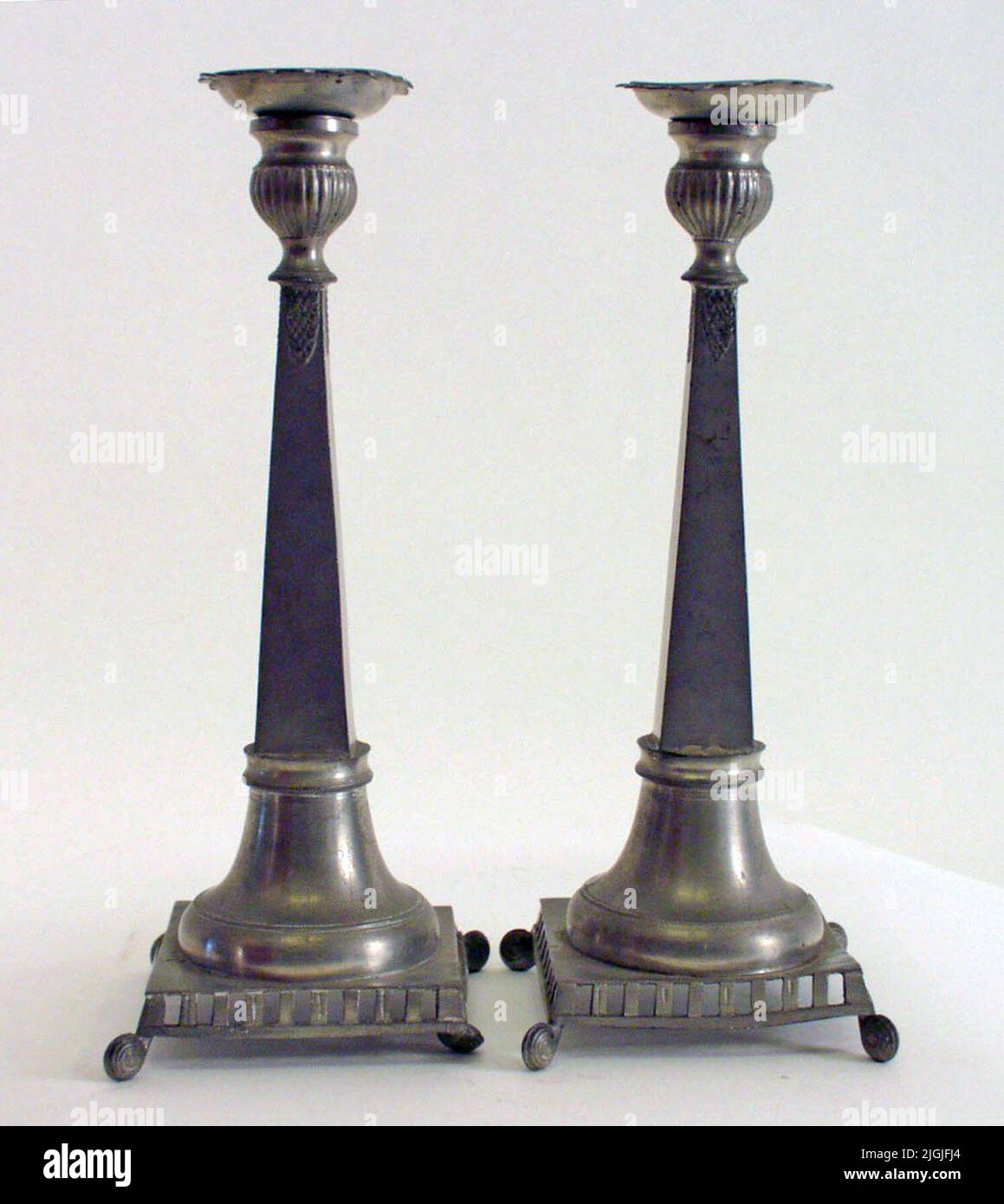 Ljusstake Candlesticks of tin, a couple. Foot of round base on square plate  with four spiral twisted feet. Rectangular penetrations on the edge of the  plate. Four -sided shaft upwards tapered. Ruffled,
