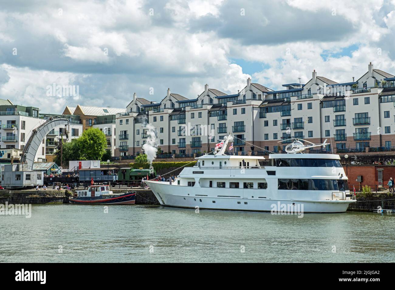The Bristol Floating Harbour featuring steam engines, an old steam crane and a large white helicoptered yacht moored up in June 2022 Stock Photo