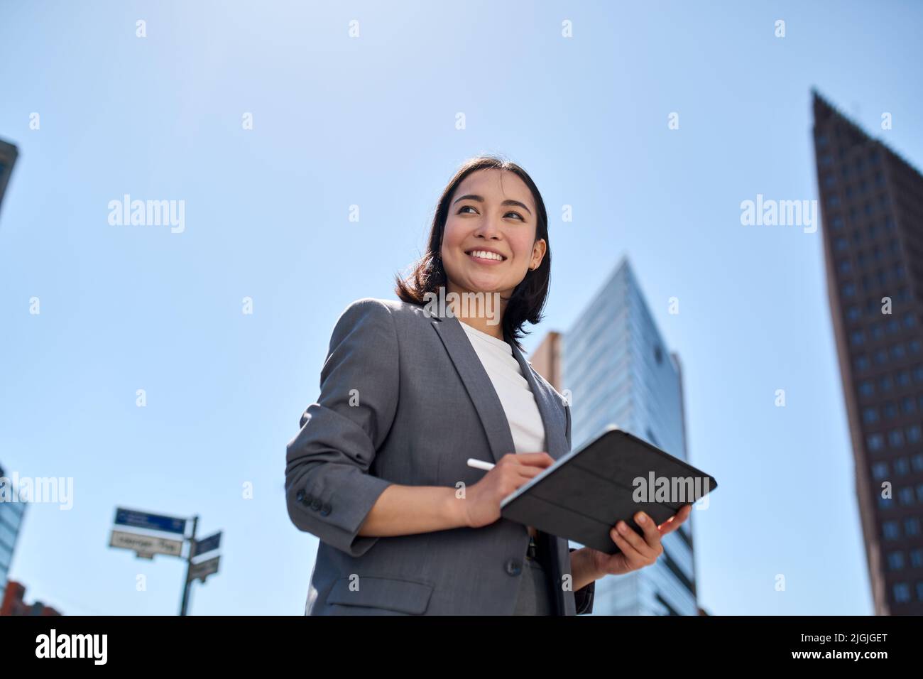 Smiling young Asian businesswoman using digital tablet on city street. Stock Photo