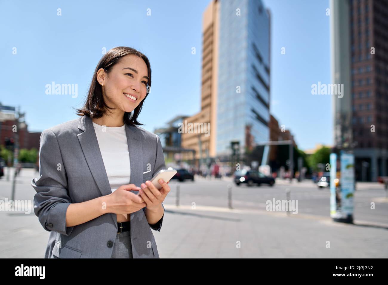 Young smiling Asian business woman using phone standing on big city ...