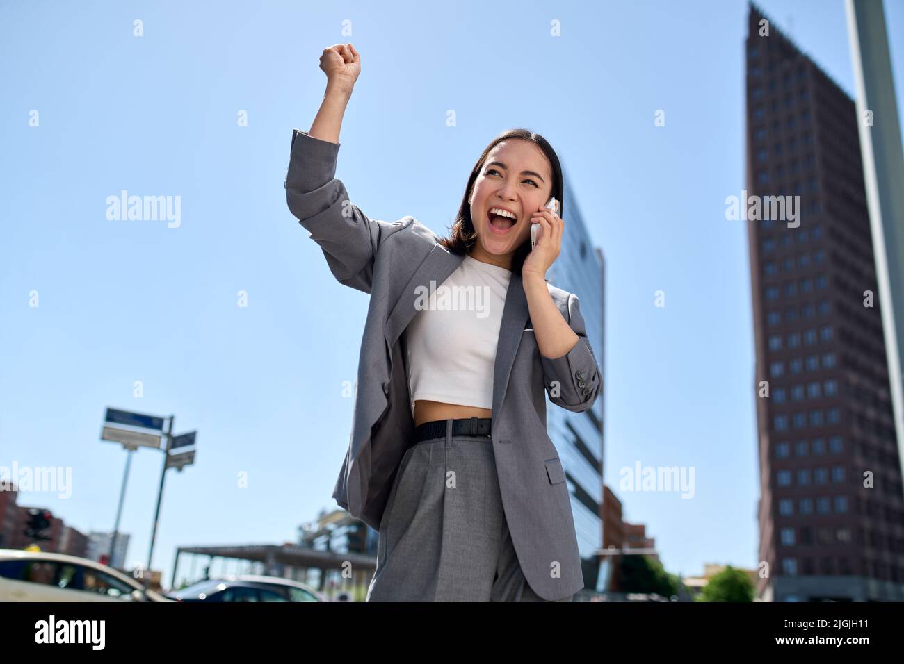Young cheerful Asian businesswoman talking on cellphone laughing on city street. Stock Photo