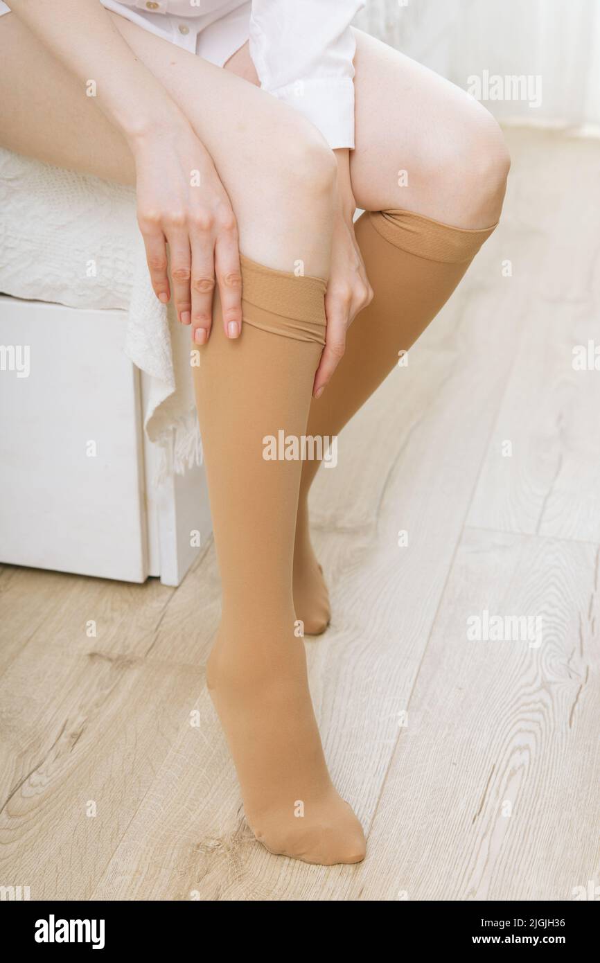 Knee socks or socks. Beige compression stockings on a woman in a white room. Girl putting on stockings at home. Beautiful female legs Stock Photo