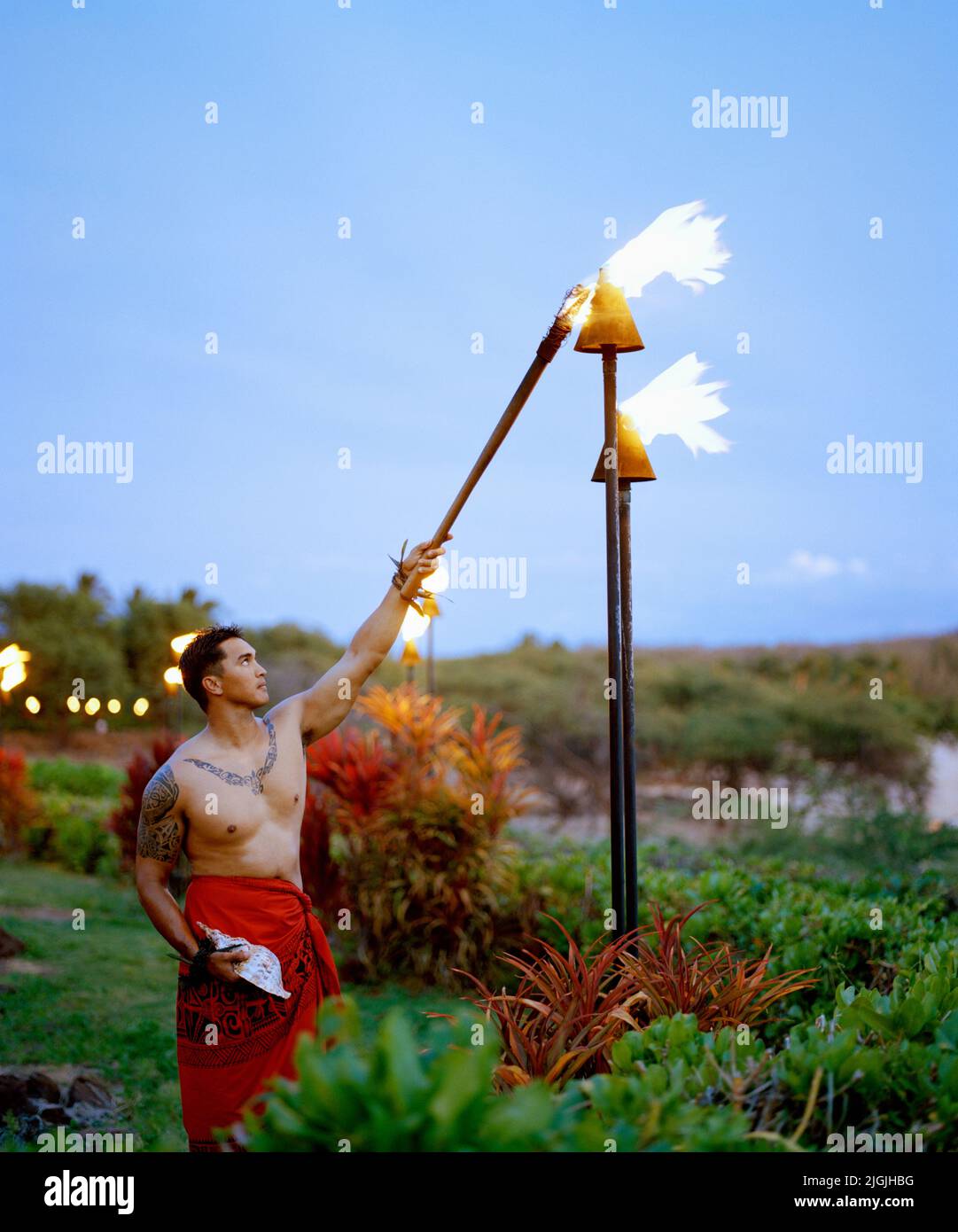 A  Hawaiian man lights torches every evening at dusk at Four Seasons Resort Lana'i at Manele Bay. Lana'i, Hawaii, USA. Stock Photo