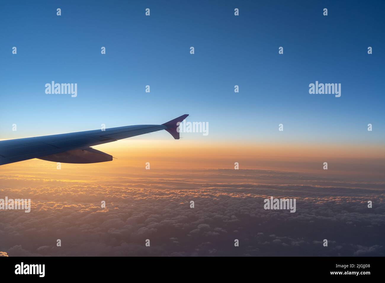 Up in the air, view of aircraft wing silhouette with dark blue sky horizon and cloud background in sun rise or sunset time from airplane window. Stock Photo