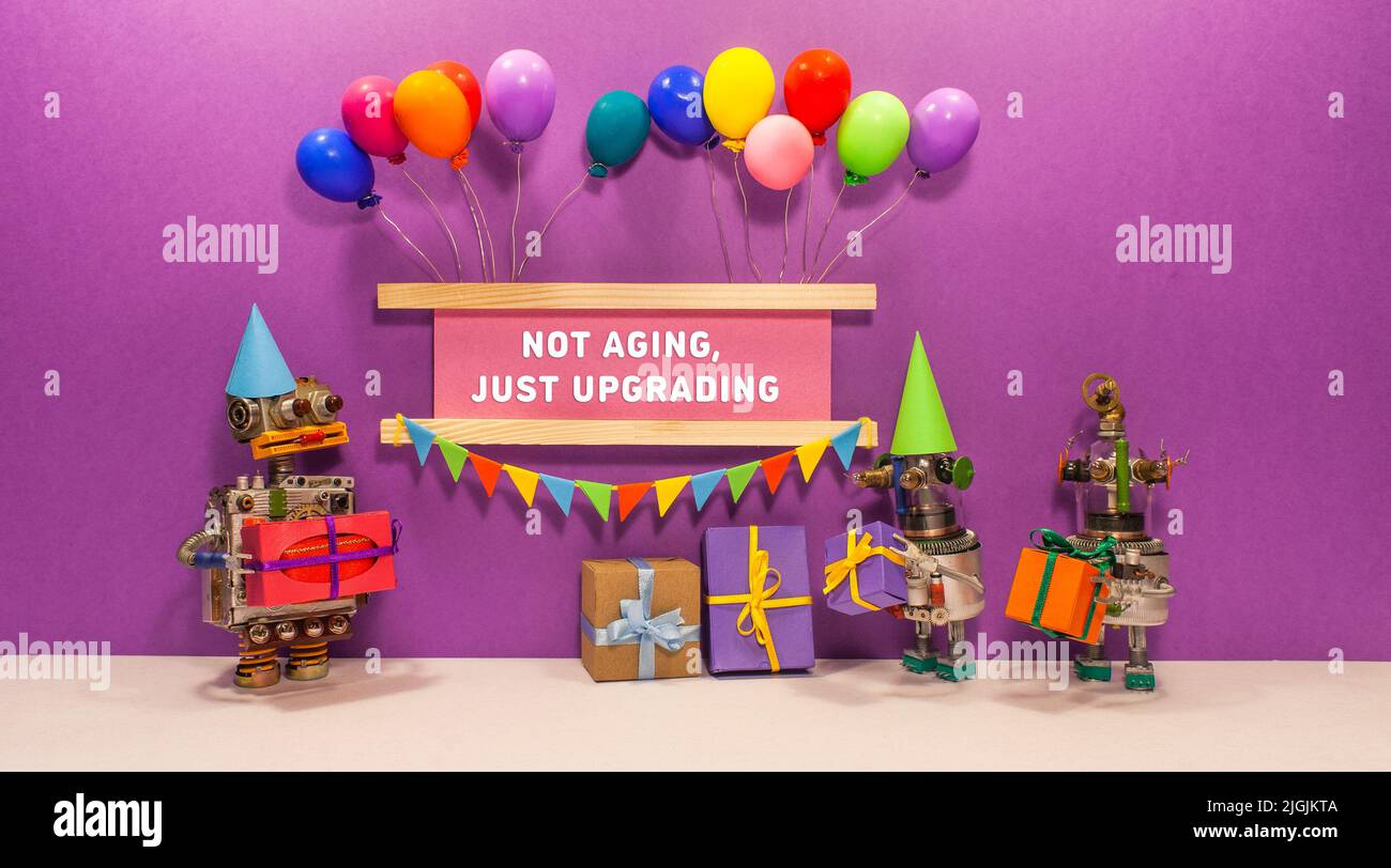 Not aging. Just upgrading. The birthday robot receives gifts from his friends. Two robots give presents cardboard boxes. banner decorated with balloon Stock Photo
