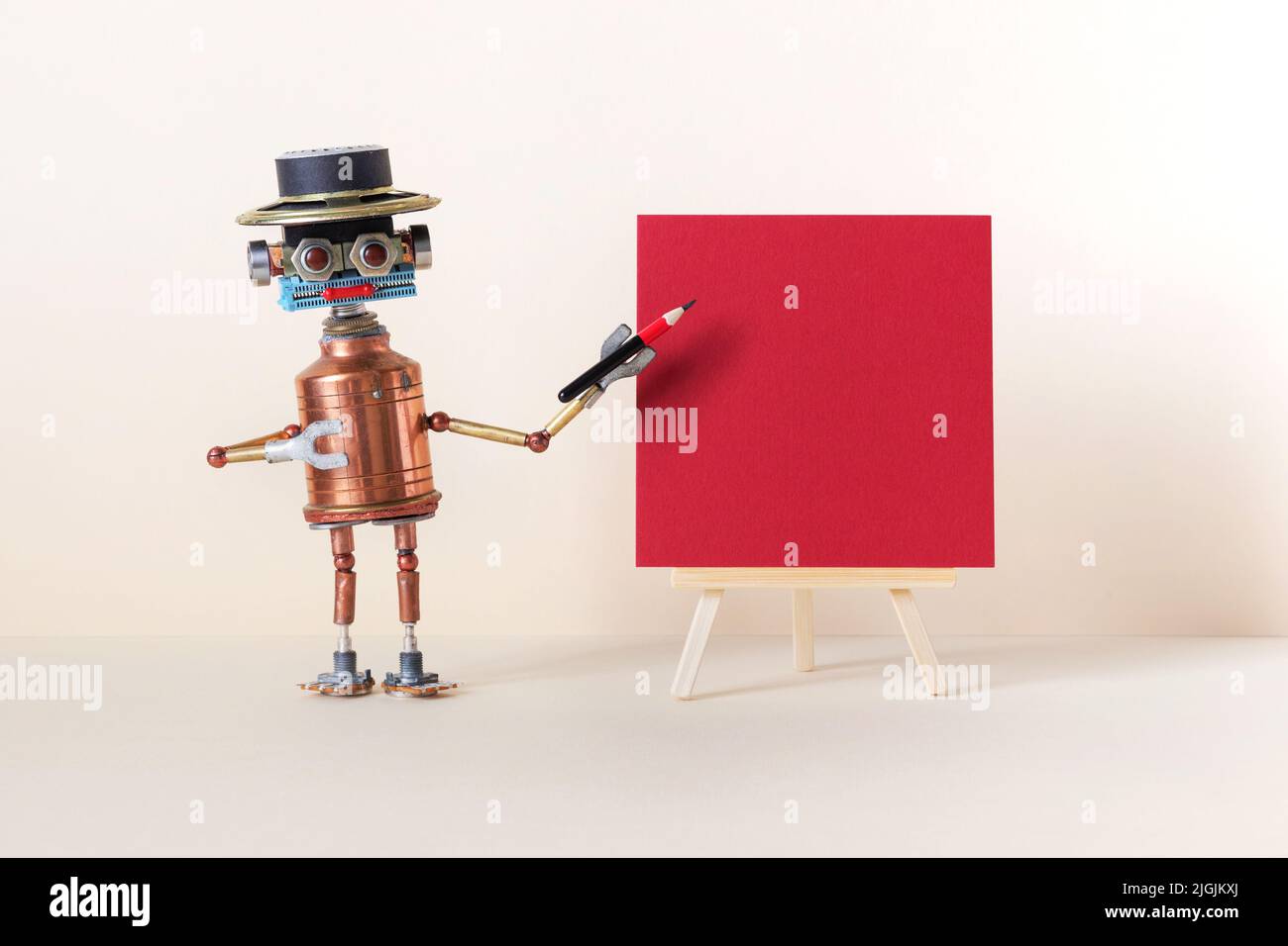 A robot artist poses with a pencil next to a wooden easel, red color paper poster. Gallery frame invitation card concept, empty frame mockup, copy spa Stock Photo