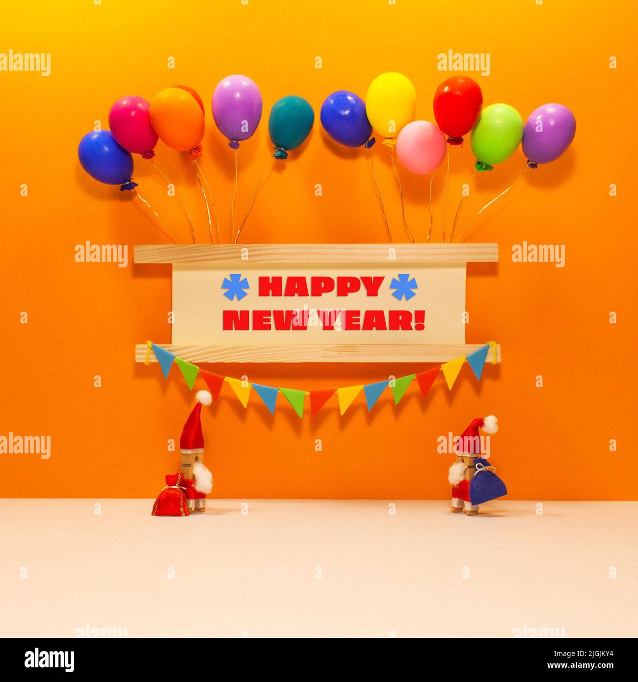 Festive sign decorated balloons, garland of flags. Two clothespin Santa Claus toys with bags of gifts. Message Happy New Year. Stock Photo