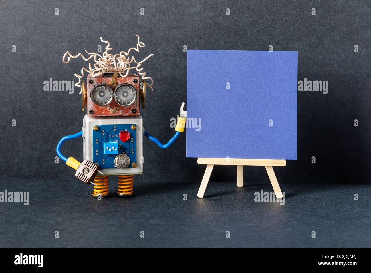 The robot and blue paper placard set on wooden easel. copy space for text. Black background. Gallery frame invitation card concept, empty frame mockup Stock Photo