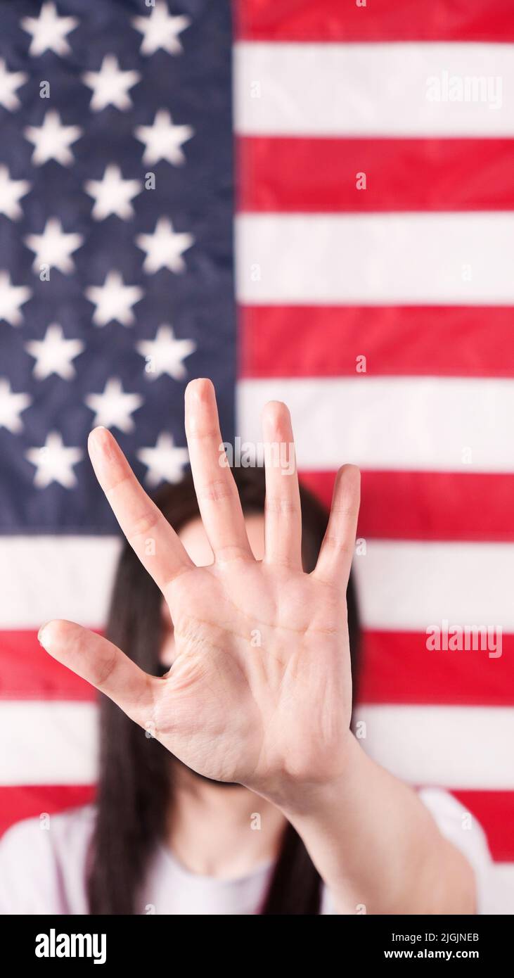 Young woman stretch out her palm to camera says stop abortion American flag on background, close up. Anti domestic violence, racism racial Stock Photo