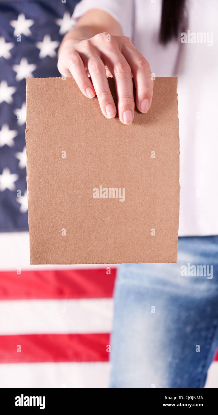 Young woman holds empty cardboard with Space for Text sign against American flag on background. Girl protesting anti-abortion laws. Feminist power Stock Photo