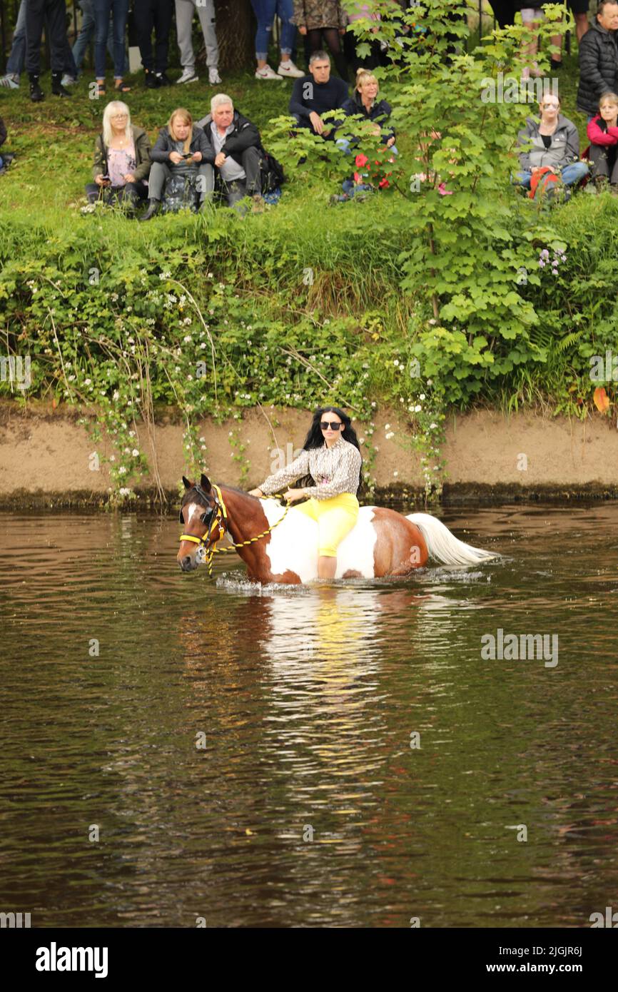 A young woman with long black hair riding a coloured horse through the River Eden, Appleby Horse Fair, Appleby in Westmorland, Cumbria Stock Photo
