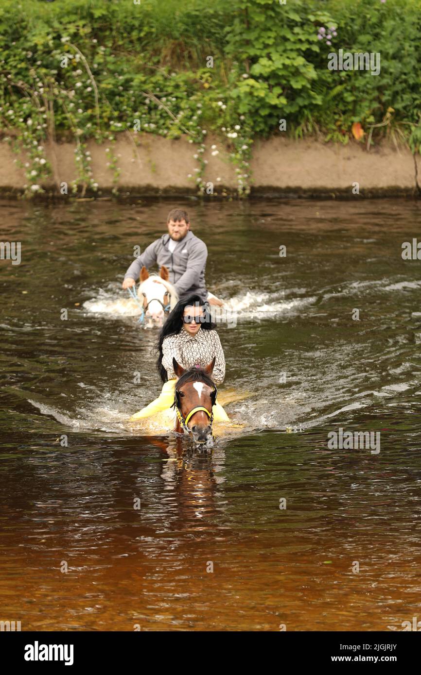 A young man and woman riding horses through the River Eden, Appleby Horse Fair, Appleby in Westmorland, Cumbria Stock Photo