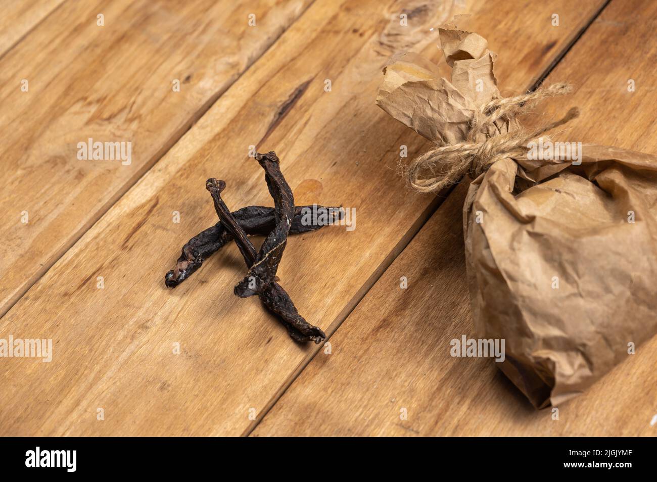 Sticks of dried meat and a paper bag against a wooden background