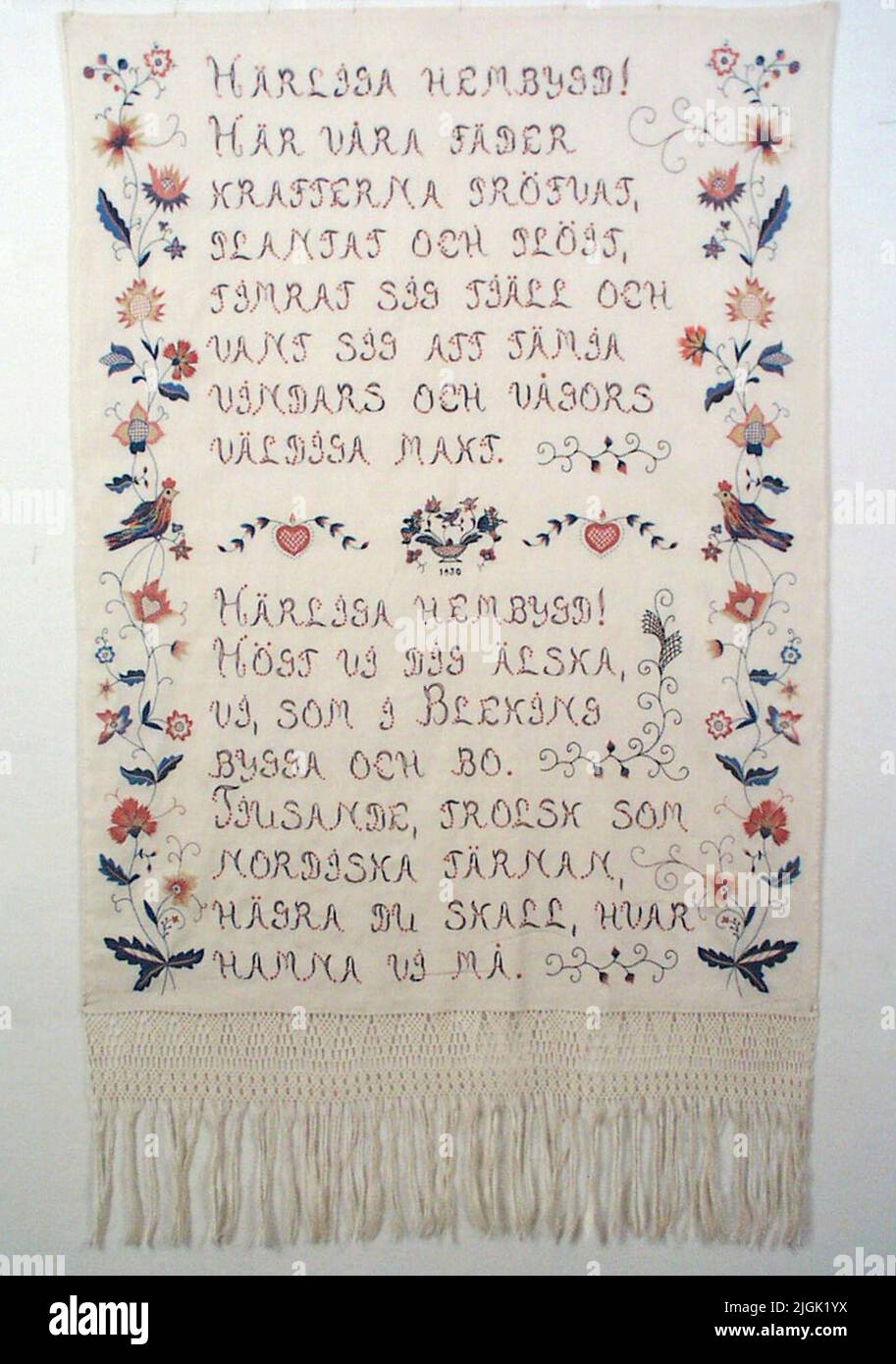 Hängkläde Hanging claw, embroidered with bleaching stitch on machine -woven linen fabric in Tuskaft: element 15 threads/cm, warp 17 threads/cm. Motiv: Text 'Lovely hometown', players. Embroidery and cotton text. Blekinge stitch: bottom stitch, stalk stitch, knots. Colors: 4 shades blue, 2 shades pink, yellow, white. The feature is in the length of the bonade. At the top of sewn suspension 12-13 mm in white semi-linen. 0.5 cm hem. Gift by Thorborg Björksten's estate. Stock Photo