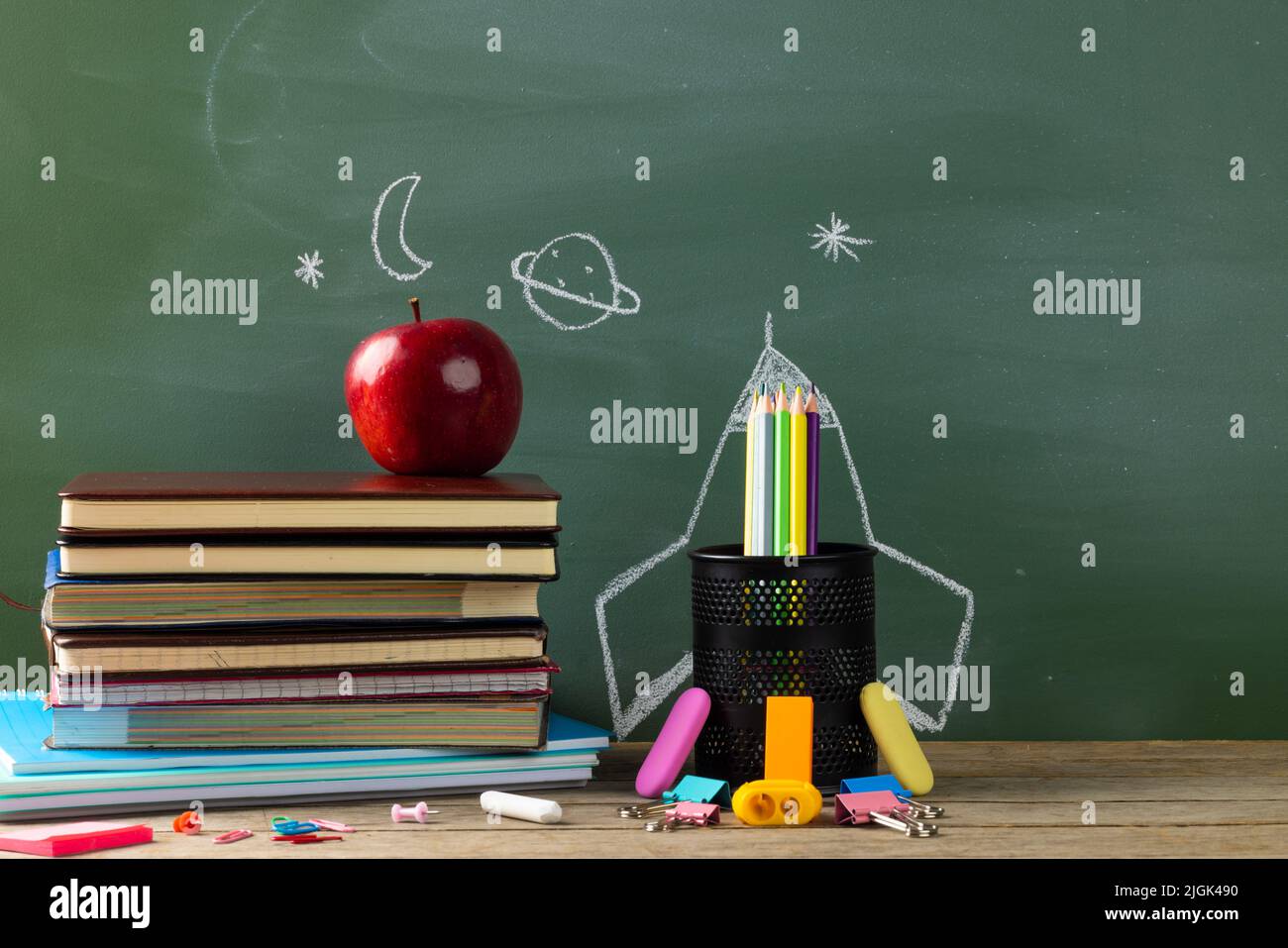 Image of school supplies, apple and notebook over drawings on black board Stock Photo