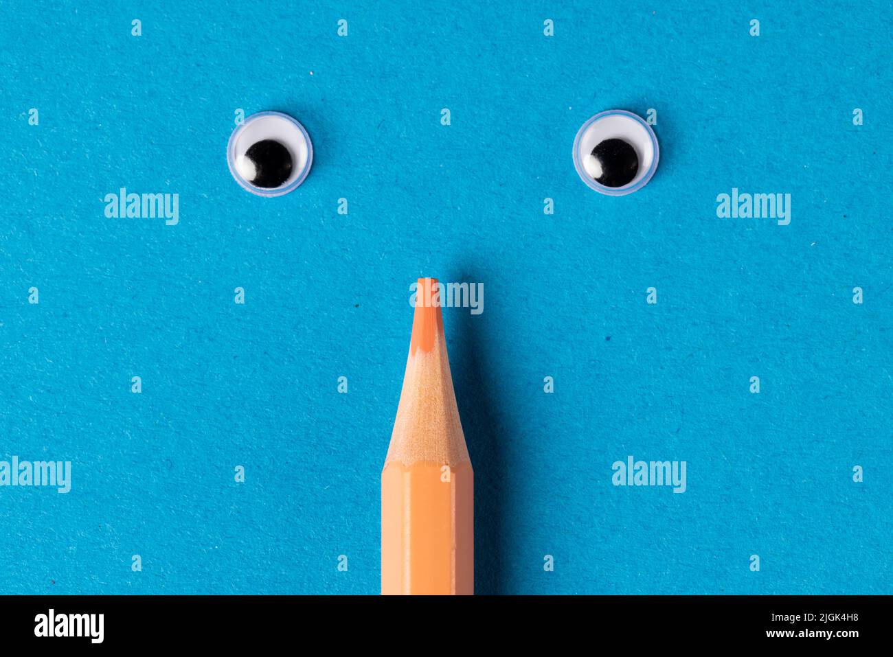 Vertical composition of crayon with eyes on blue surface Stock Photo