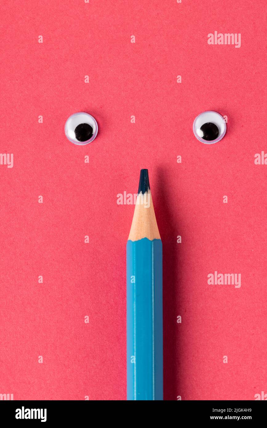Vertical composition of pencil with eyes on blue surface Stock Photo