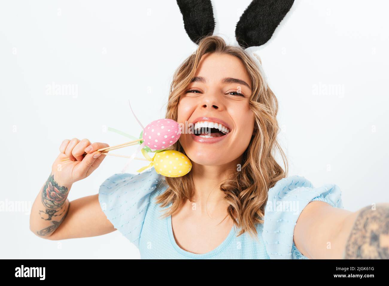 Pretty young woman wearing Easter bunny ears and holding colored eggs ...