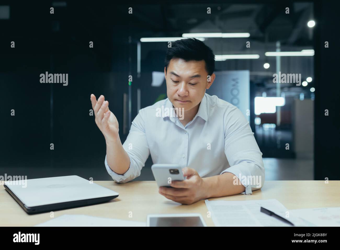 Upset asian businessman working in office, reading bad news on phone, man depressed at work Stock Photo