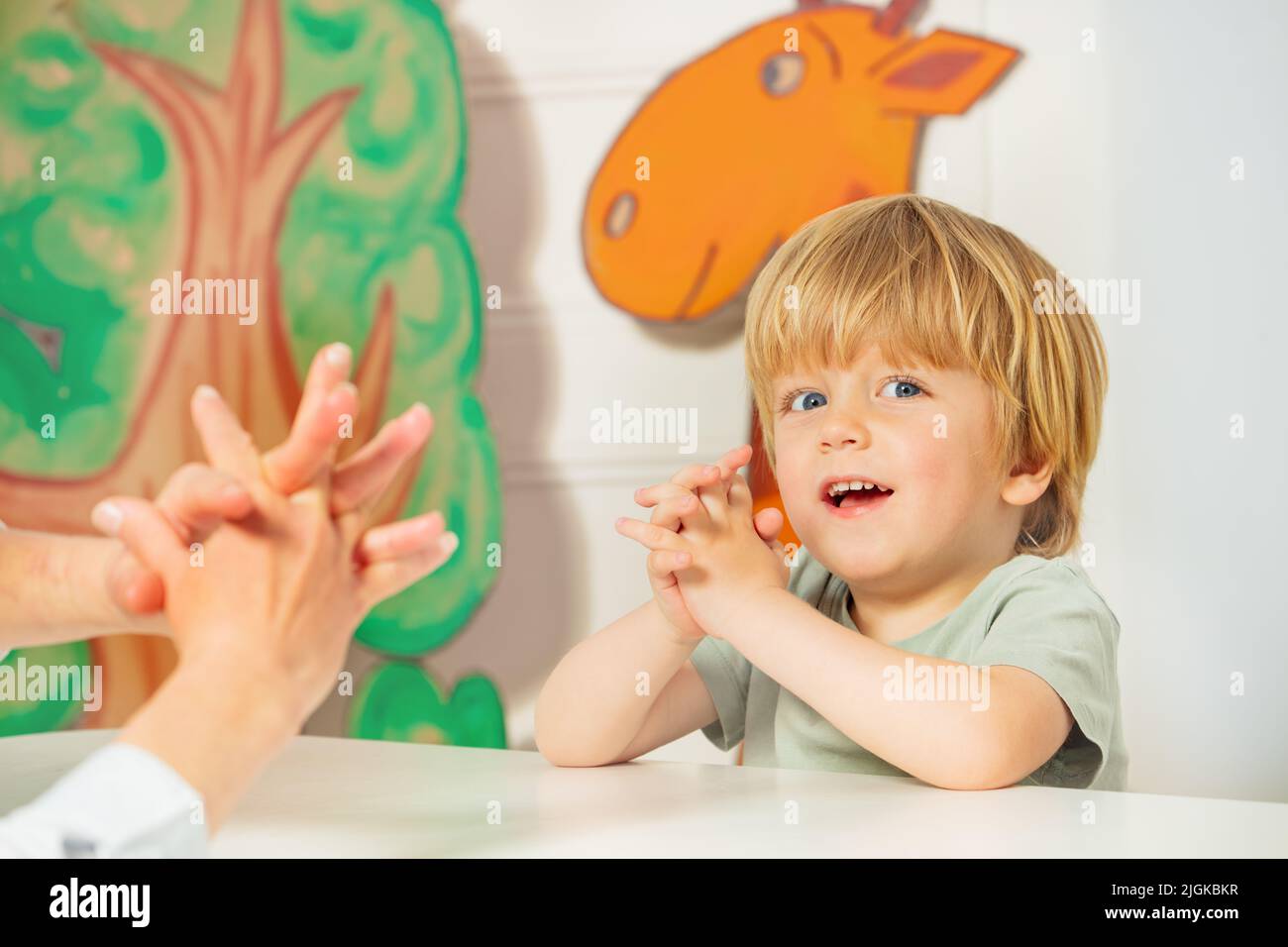 Little blond boy play finger game sitting by the desk in class Stock Photo