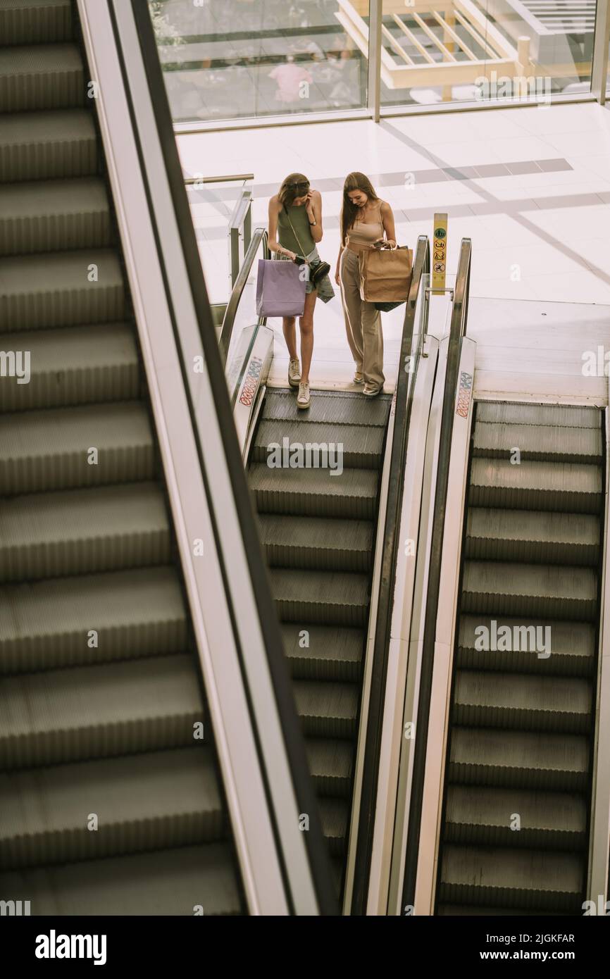 Beautiful girls with their phones going down on the escalator Stock