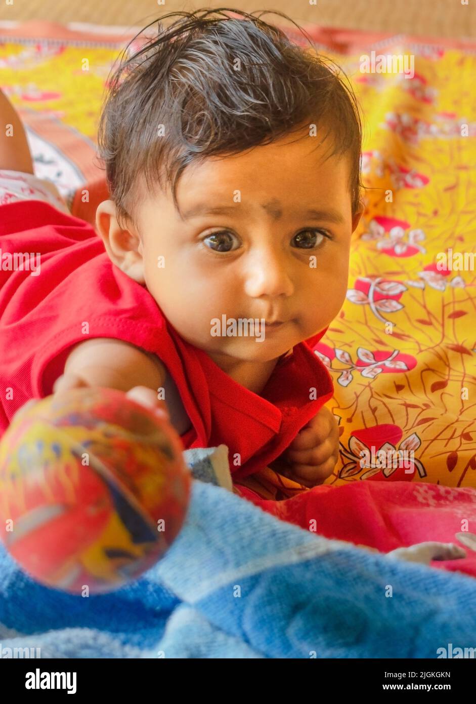 A cute Indian baby holding a ball towards the camera while lying down