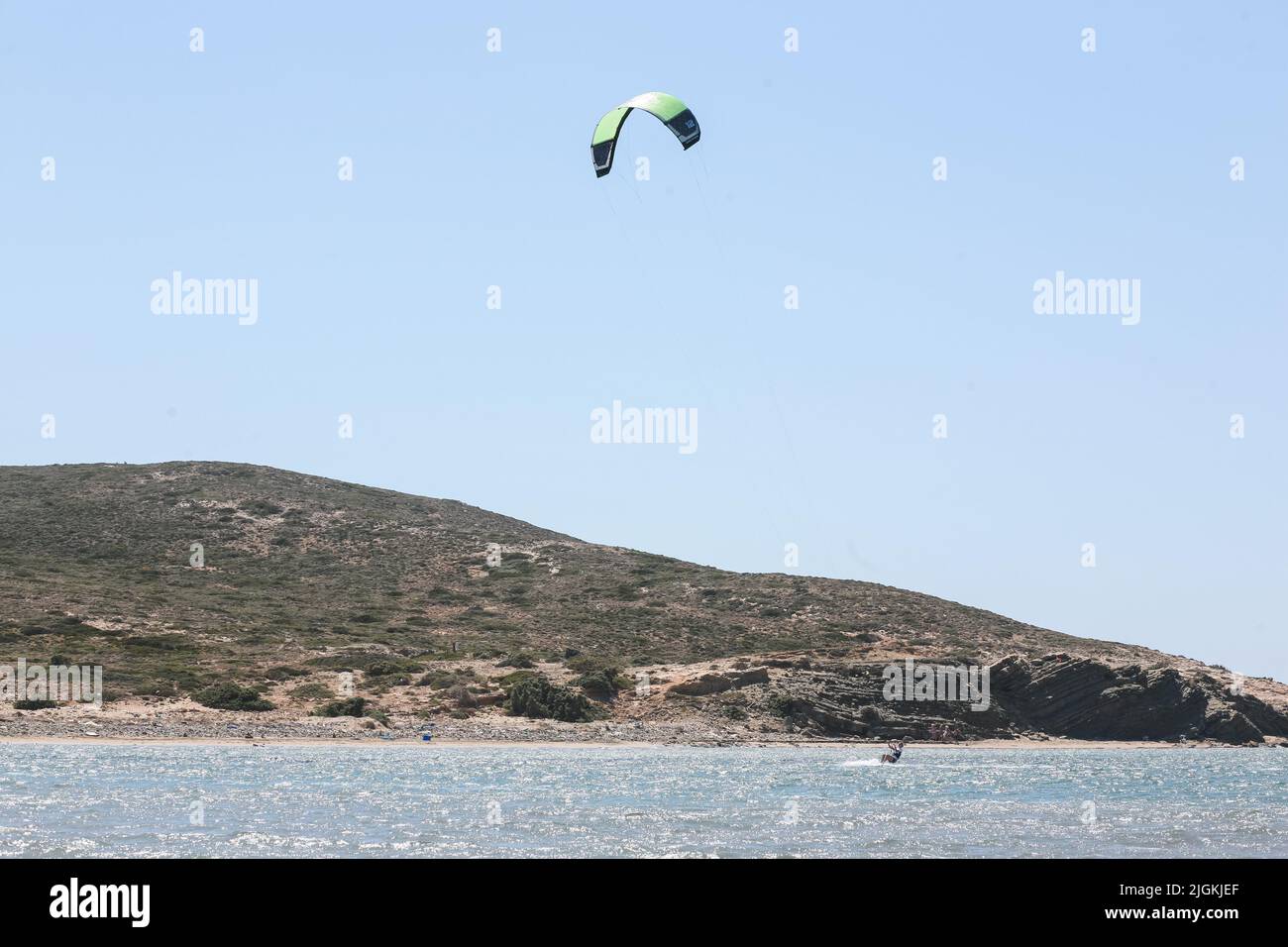 Professional kite surfer rides on a board with a plank on a lake with sea water at sunset. Water splashes and sun glare. Water sports. Panoramic view Stock Photo