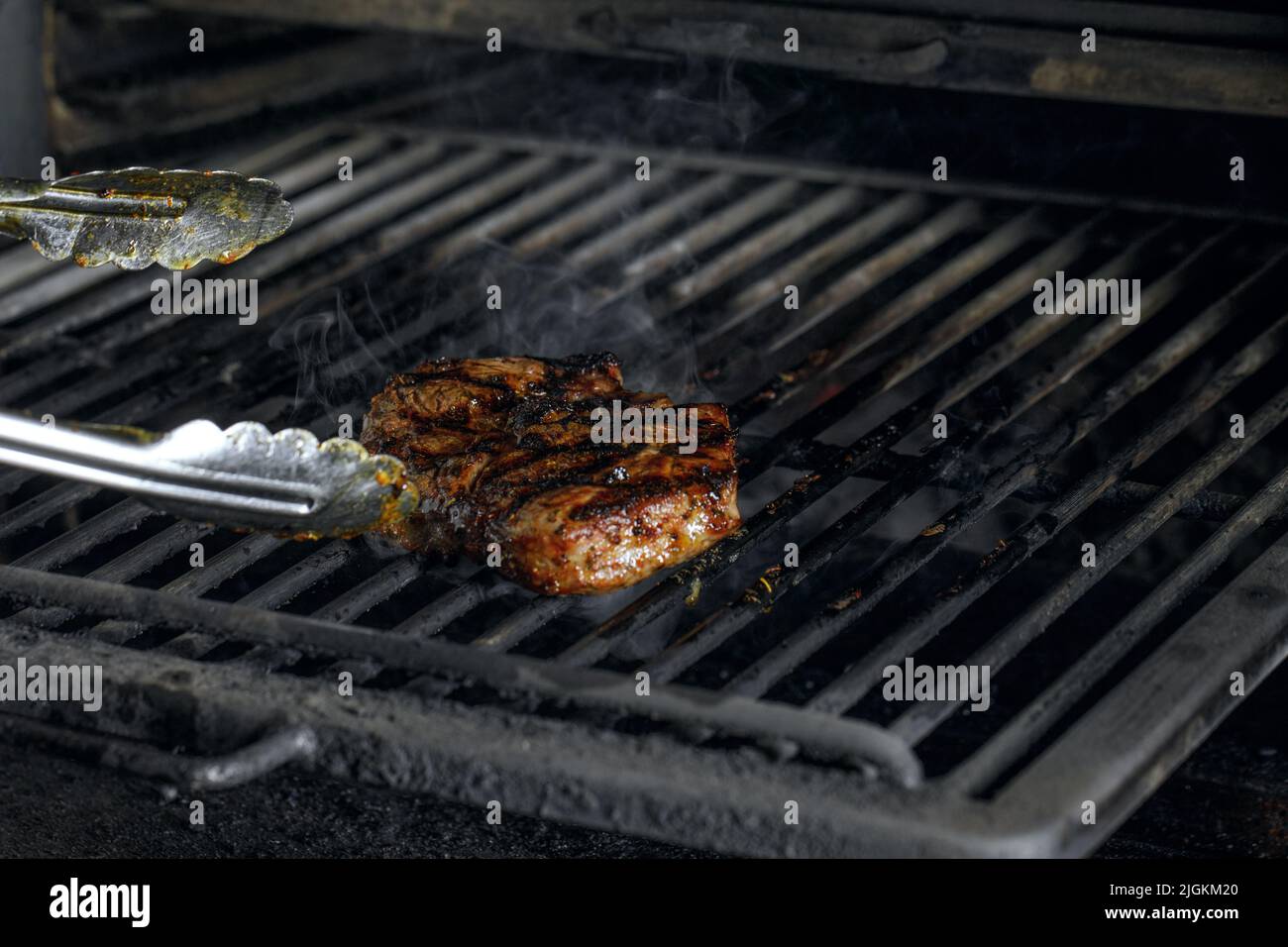 roasted meat beef steak grilling on rack charcoal stove with smoke on black background Stock