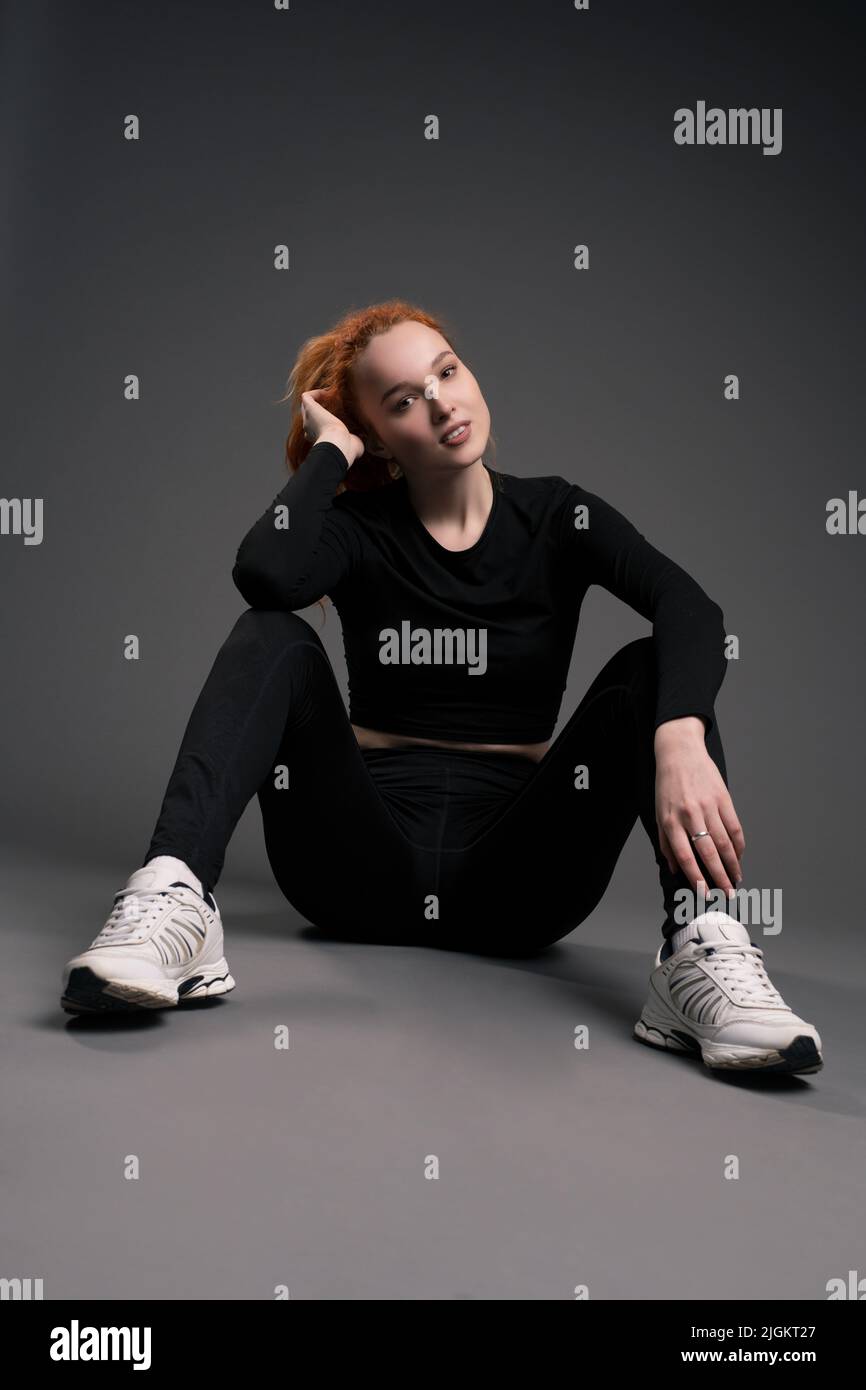 Smiling redhead young sportswoman resting on floor in studio Stock Photo