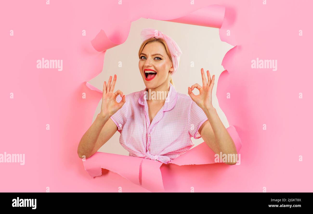 Smiling girl shows sign ok looking through paper hole. Woman gesturing okay. Discount. Sale. Stock Photo